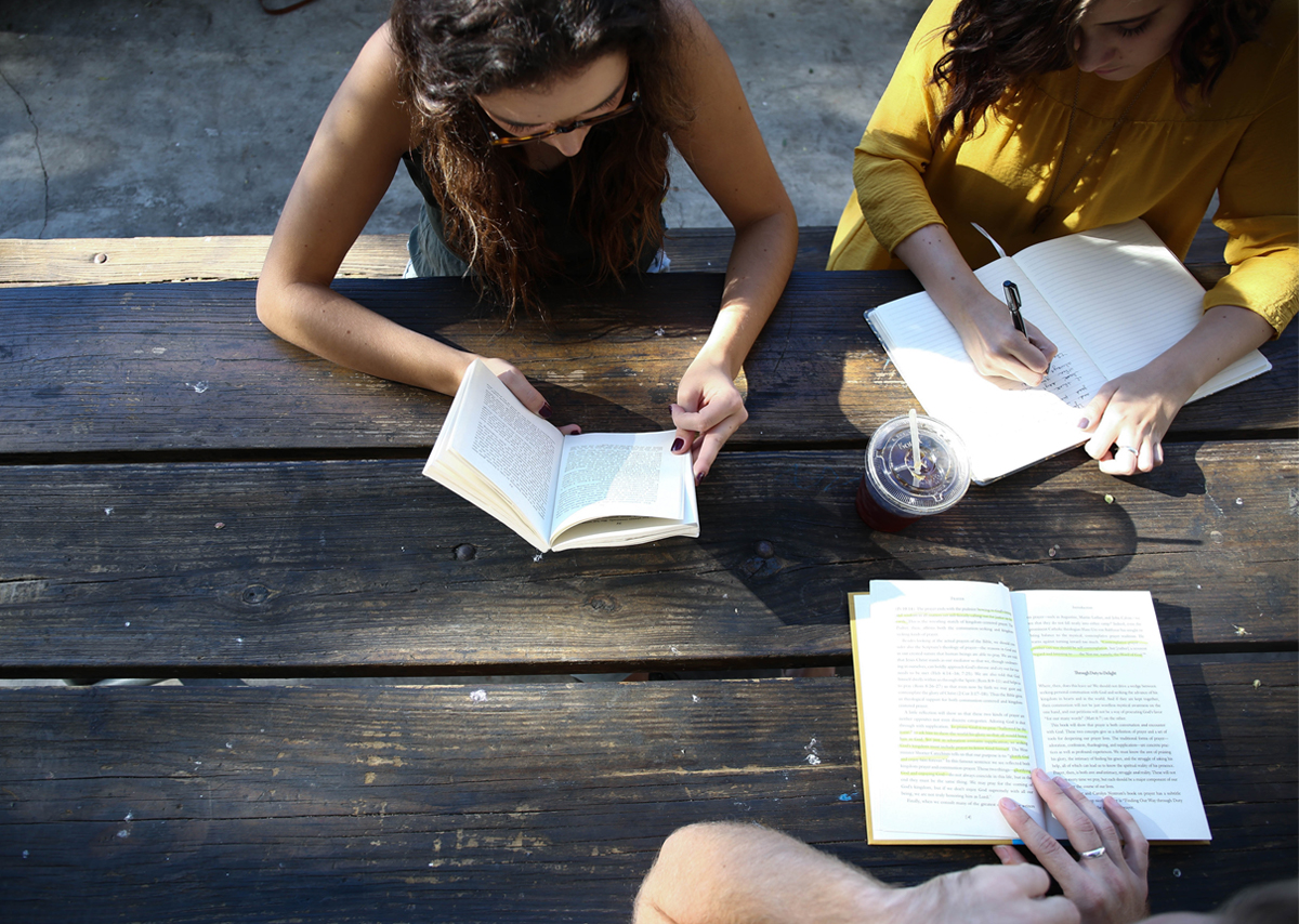 Two college girls studying at a picnic table outside with their notebooks and pens