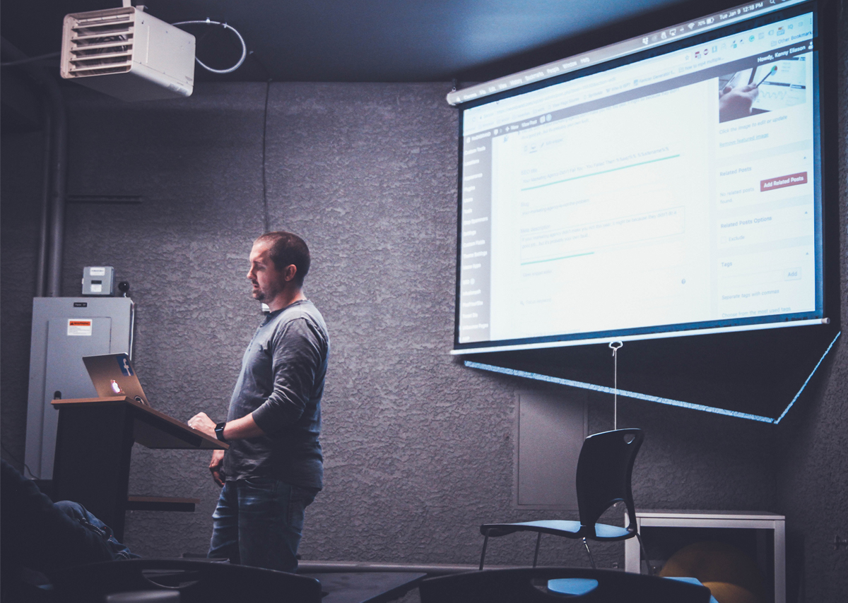 A professor teaching a college class in front of a projector screen