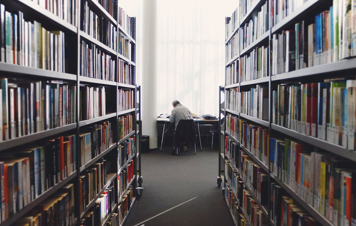 A student studying at a desk in the university library with shelves of books on either side