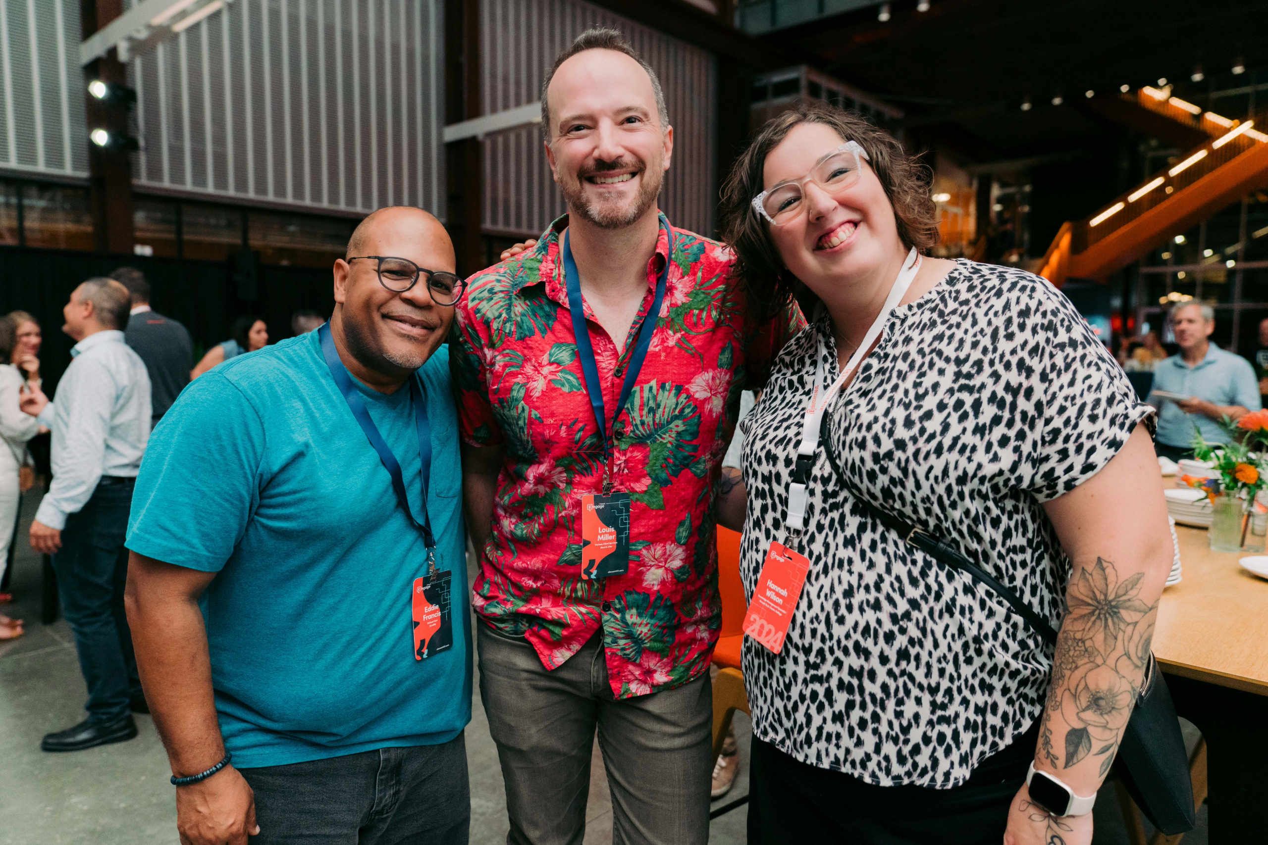 Three people at the Engage Summit 2024. (L-R) Eddie Francis, a shorter dark-skinned bald man wearing a teal blue t-shirt. In the middle, Louis Miller, a tall light-skinned man with dark hair and salt and pepper beard wearing a green and red floral button-up shirt. Hannah Wilson a tall light-skinned woman with shoulder length dark curly hair wearing glasses and a leopard print top.