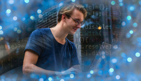 Higher ed administration gets AI boost article image. A young man wearing glasses and a casual blue t-shirt is smiling while working on a laptop. The image has a futuristic feel, with overlaid lines of programming code and a blurred blue bokeh effect, symbolizing technology, coding, and artificial intelligence.